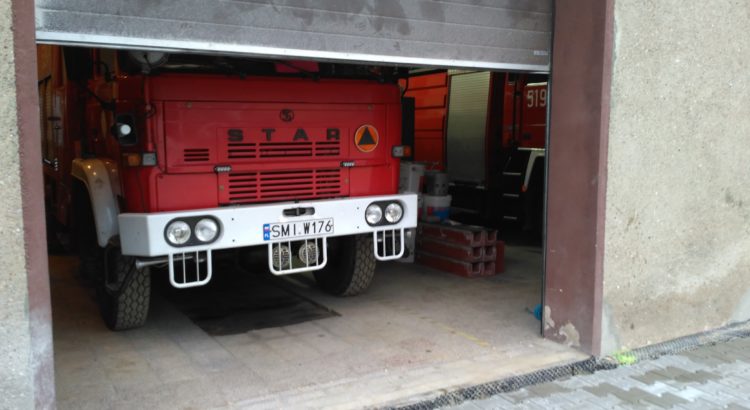 Wóz gaśniczy GBA 2,5/16 marki Star stoi w garażu, którego brama się otwiera.